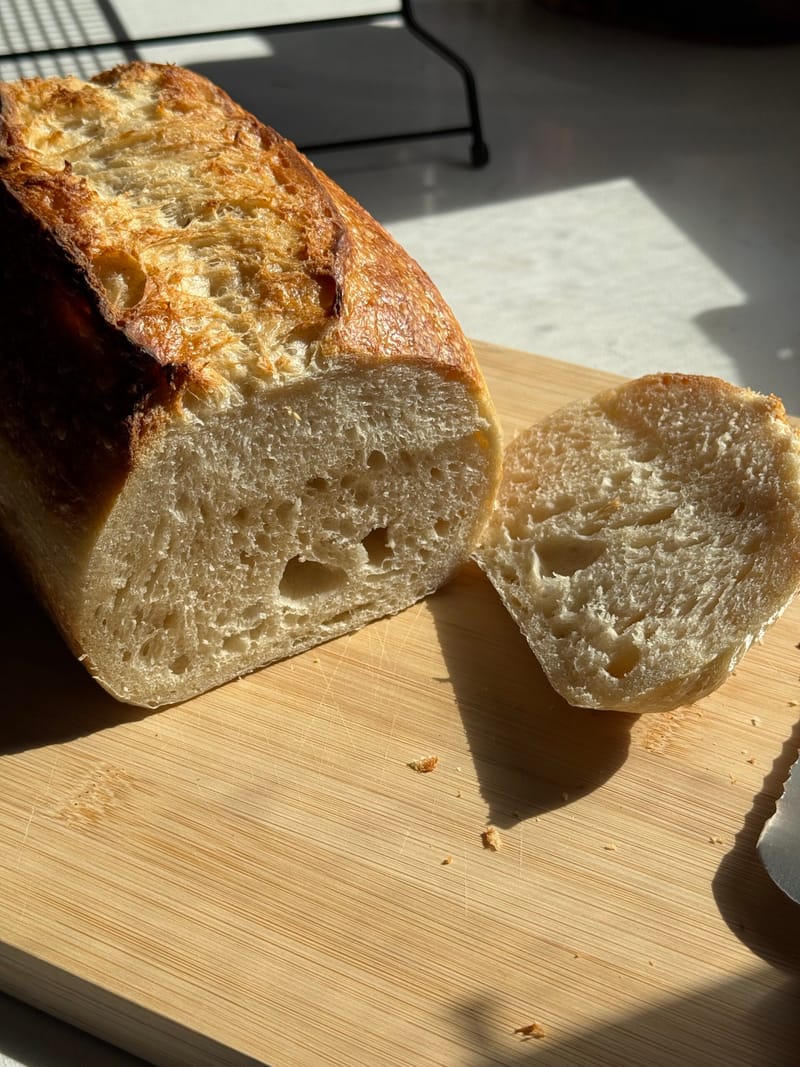 A sourdough loaf sliced open on a wooden board, showing an open, airy crumb