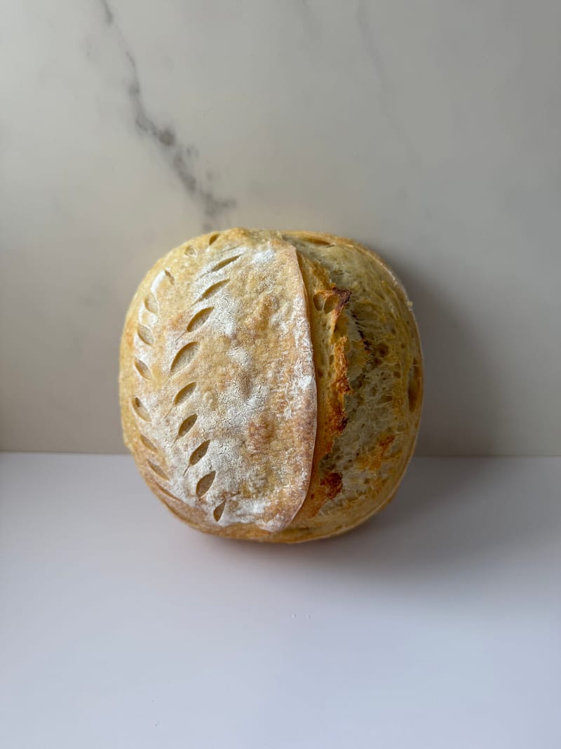 A scored sourdough boule with a golden, flour-dusted crust on a marble counter